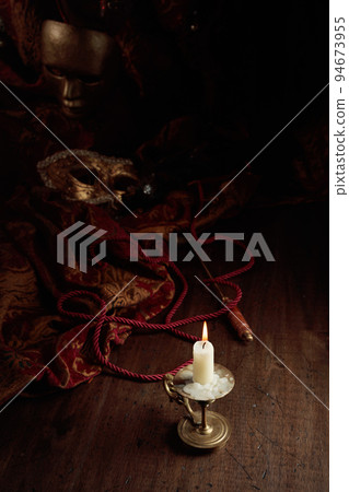 Burning candle in an old brass candlestick and carnival masks. Burning candle in an old brass candlestick and carnival masks. 94673955