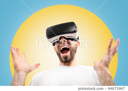 A wondered caucasian man in virtual reality glasses, with his mouth slightly open, spreads his hands. Blue background with a yellow circle. The concept of virtual reality 94673967