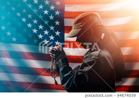 Memorial day, veterans day. A young woman holds a rosary in her hands and prays. American flag on the background. Copy space. Concept of American holidays and religion. 94674039
