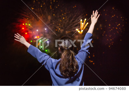 A young brunette woman enjoys the fireworks in the sky.Concept of festivals and holidays with fireworks. The view from the back A young brunette woman enjoys the fireworks in the sky.Concept of festivals and holidays with fireworks. The view from the back 94674080