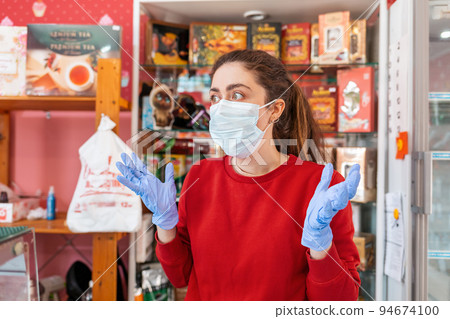 A woman in rubber gloves and a medical mask throws her hands out in fright. In the background-shelves and shop Windows. The concept of coronovirus, quarantine and crisis in business 94674100