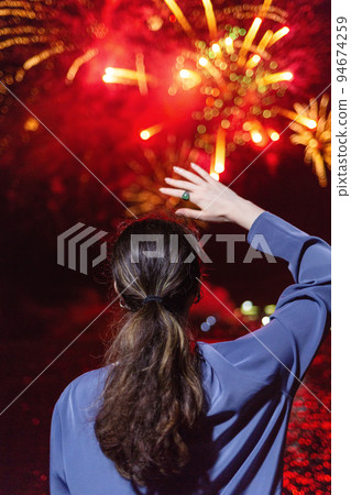 A young woman enjoys the fireworks in the sky.Concept of festivals and holidays with fireworks. The view from the back. Close up A young woman enjoys the fireworks in the sky.Concept of festivals and holidays with fireworks. The view from the back. Close up 94674259