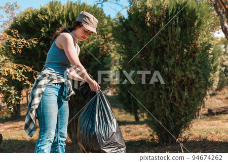 The concept of environmental pollution and Earth day. A female volunteer cleans the Park, collecting garbage bags in one place. Close up The concept of environmental pollution and Earth day. A female volunteer cleans the Park, collecting garbage bags in one place. Close up 94674262