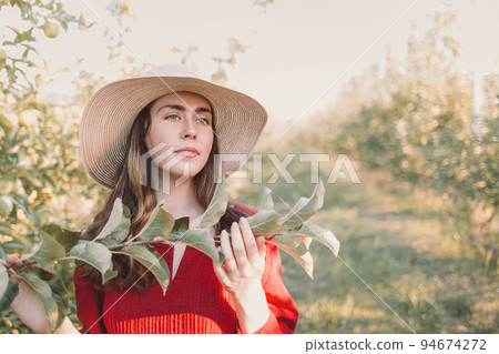 Portrait in garden. Young and beautiful woman in a hat and a red dress, with a tree branch in her hands.Copy space Portrait in garden. Young and beautiful woman in a hat and a red dress, with a tree branch in her hands.Copy space 94674272