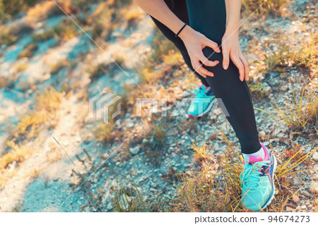 A young athletic woman is experiencing pain in her leg due to an injury while Jogging on rough terrain. Concept of sports and sports injuries. Copy space A young athletic woman is experiencing pain in her leg due to an injury while Jogging on rough terrain. Concept of sports and sports injuries. Copy space 94674273