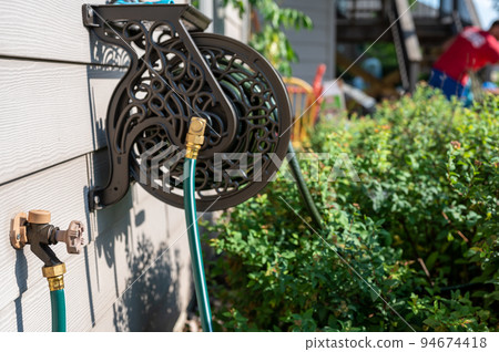 Decorative metal hose storage wheel mounted on the exterior of a residential house.  94674418