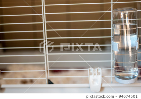 Selective focus on a water bottle mounted on the bars of a small animal cage.  94674501