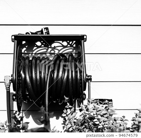 Decorative metal hose storage wheel mounted on the exterior of a residential house.  94674579