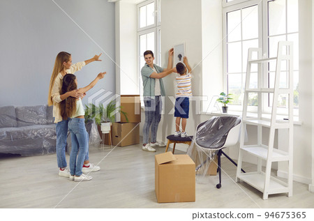 Happy family are hanging picture on wall while decorating their newly bought house Happy family are hanging picture on wall while decorating their newly bought house 94675365