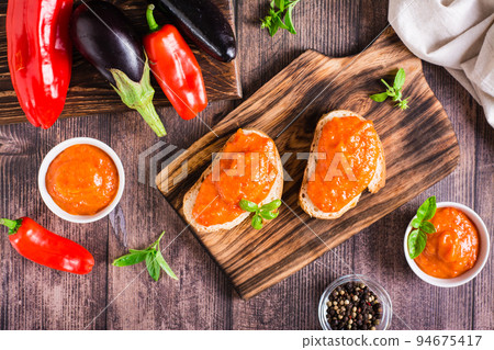 Ajvar delicious appetizer of pepper, eggplant and garlic on bread and in bowls. Top view Ajvar delicious appetizer of pepper, eggplant and garlic on bread and in bowls. Top view 94675417