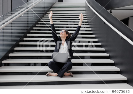 business woman in a strict suit with a laptop in the office of the business center is sitting on the steps rejoicing at a successful contract victory business woman in a strict suit with a laptop in the office of the business center is sitting on the steps rejoicing at a successful contract victory 94675685