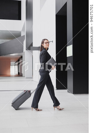 business tourism, business woman in a formal suit with a smartphone in a business center or airport with a suitcase goes on a business trip business tourism, business woman in a formal suit with a smartphone in a business center or airport with a suitcase goes on a business trip 94675701