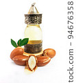 Argan oil in a oriental glass and metal bottle and argan nuts with green leaves isolated on white background. 94676358