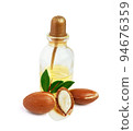 Three argan nuts with green leaves glass bottles on isolated white background. Chopped argan nut with a drop of oil. Whole and half Moroccan Argania Spinosa seeds for the production of oil 94676359