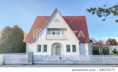 A private house of two floors with triangular roof and an area near the house against a blue sky A private house of two floors with triangular roof and an area near the house against a blue sky 94676571