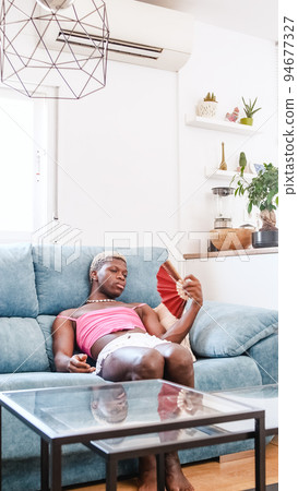 Displeased transsexual black person suffering from heat on couch at home Displeased transsexual black person suffering from heat on couch at home 94677327