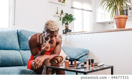African black person with red lips drawing line under eye during makeup application 94677331