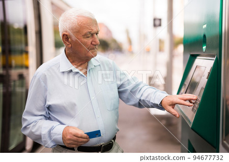 Old man using cash machine on tram station 94677732