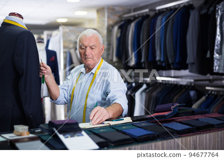 Mature tailor makes measurements of business suit at studio Mature tailor makes measurements of business suit at studio 94677764