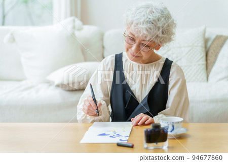 Gray-haired woman writing a letter in the living room 94677860