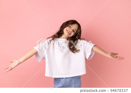 Portrait of positive optimistic little girl wearing white T-shirt inviting to embrace, keeping hands as giving, sharing for free. Indoor studio shot isolated on pink background. 94678337