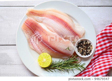 fresh raw pangasius fish fillet with herb and spices lemon lime and rosemary, meat dolly fish tilapia striped catfish, fish fillet on white plate with ingredients for cooking - top view 94679347