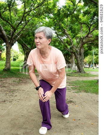 A 60-year-old Asian mature woman stretches her thighs and thighs, enjoys the fresh air of nature in the park. 94681629