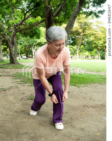 一位60歲的亞洲成熟女性伸展著大腿和大腿，在公園裡享受著大自然的新鮮空氣。 94681647