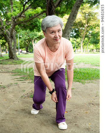 一位60歲的亞洲成熟女性伸展著大腿和大腿，在公園裡享受著大自然的新鮮空氣。 94681655