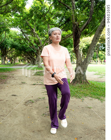 A 60-year-old Asian mature woman stretches her thighs and thighs, enjoys the fresh air of nature in the park. 94681695