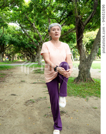 A 60-year-old Asian mature woman stretches her thighs and thighs, enjoys the fresh air of nature in the park. 94681696