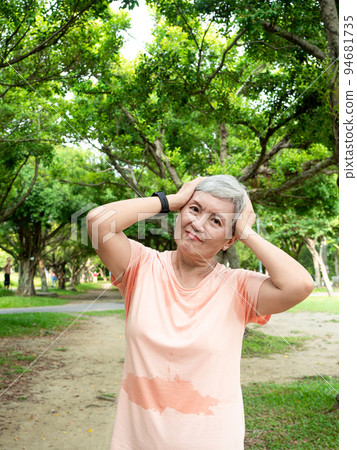 一位 60 歲的亞洲成熟女性在戶外公園裡抱著頭。 一位 60 歲的亞洲成熟女性在戶外公園裡抱著頭。 94681735