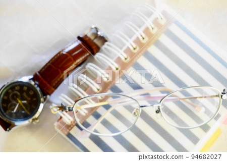 A notebook, glasses, and a wristwatch on a white table A notebook, glasses, and a wristwatch on a white table 94682027