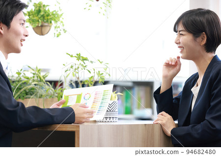 一位男性藝術總監和一位女性設計師 2 一邊開會一邊看著配色方案提案和打印的顏色圖表 94682480
