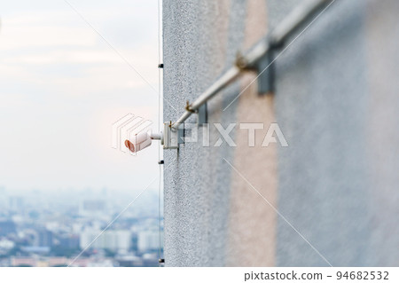 Modern CCTV camera against city and sky background. surveillance, video record and monitoring concept Modern CCTV camera against city and sky background. surveillance, video record and monitoring concept 94682532