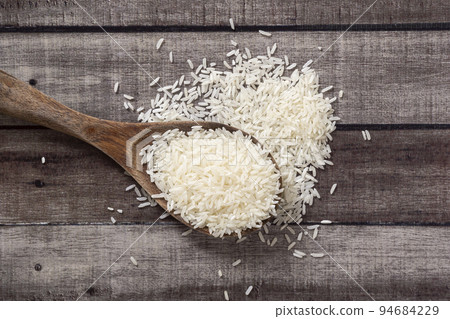 Closeup uncooked dry Thai jasmine rice are overflow from a wooden ladle on wooden floor, angle of view flat lay and top down horizontal view. Closeup uncooked dry Thai jasmine rice are overflow from a wooden ladle on wooden floor, angle of view flat lay and top down horizontal view. 94684229