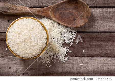 Uncooked dry Thai jasmine rice are overflow from a bowl and wooden ladle beside put on wood floor, angle of view flat lay and top down horizontal view. Uncooked dry Thai jasmine rice are overflow from a bowl and wooden ladle beside put on wood floor, angle of view flat lay and top down horizontal view. 94684379