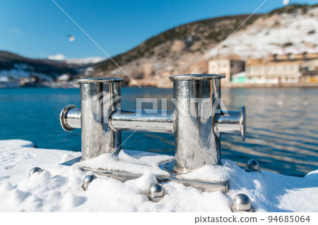 A metal cnecht is covered with snow on a pier in Balaklava in winter. Winter landscape of the seaside town in Crimea 94685064