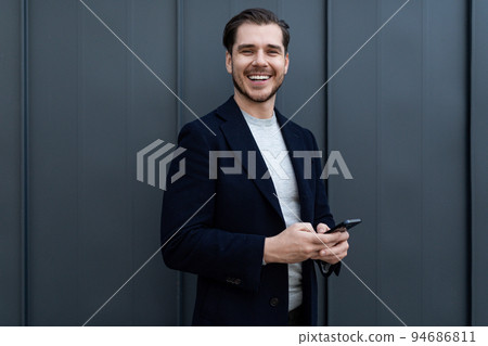 portrait of a strong middle-aged businessman using a mobile phone and a wide smile against a gray 94686811