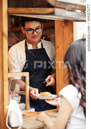 Smiling barista giving customer fresh croissant on small plate Smiling barista giving customer fresh croissant on small plate 94687077