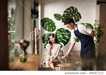 Coffeeshop waiter bringing cup of coffee to young woman talking on phone 94687113
