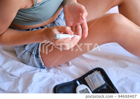 Teenage girl measures blood sugar level on the bed at home. 94688407