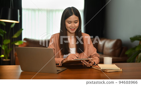 Attractive millennial businesswoman sitting front of laptop and using digital tablet on wooden table 94688966