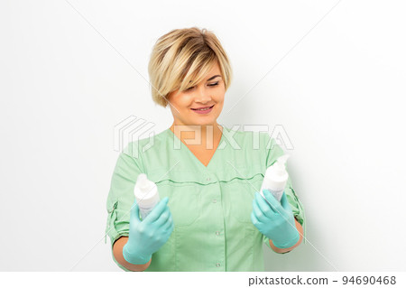 Cosmetics creams and skin care products in the hands of the female beautician smiling and standing over the white wall background 94690468