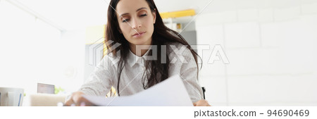 Tired overworked young woman go through paper on working place 94690469