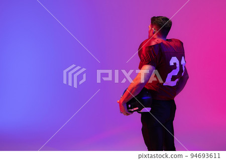 Caucasian male american football player holding helmet with neon pink and blue lighting Caucasian male american football player holding helmet with neon pink and blue lighting 94693611