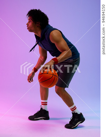 Image of biracial basketball player with basketball on purple to blue background 94694150