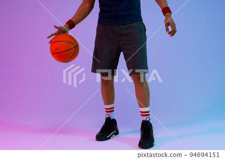 Image of low section of biracial basketball player with basketball on purple to blue background 94694151
