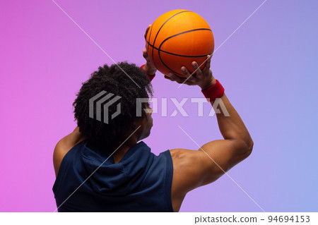 Image of biracial basketball player throwing basketball on purple to blue background 94694153