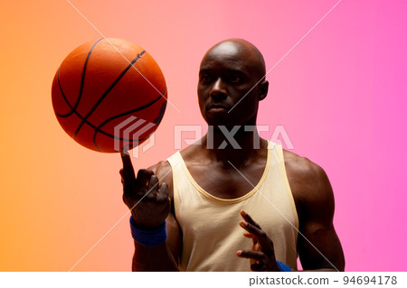 Image of african american basketball player playing with basketball on orange to pink background 94694178